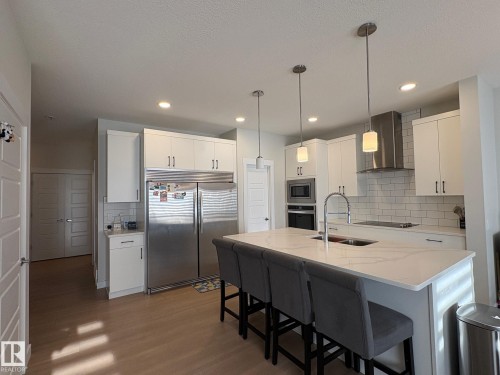 Modern kitchen featuring a large center island with integrated sink, white cabinetry, stainless steel appliances, and wood-finish flooring - 9952 227 Street, Edmonton, AB 