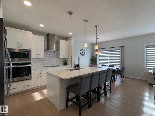 Kitchen featuring white cabinetry, subway tile backsplash, stainless steel appliances, and an island with a built-in sink - 9952 227 Street, Edmonton, AB 