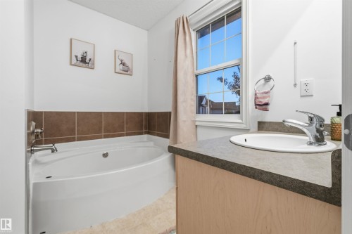Bathroom featuring a built-in corner soaking tub with brown tile surround, a single window, and a vanity with an integrated sink and gray countertop - 21207 90Ave, Edmonton, AB 
