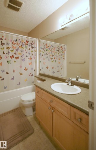 Bathroom featuring a single vanity with wood-finish cabinetry, a solid surface countertop, an undermount sink, and a chrome faucet - 21207 90Ave, Edmonton, AB 