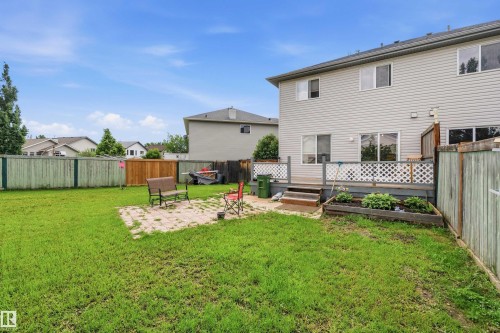 Expansive fenced backyard featuring a wood deck, sliding glass doors, a paver patio, and raised garden beds - 21207 90Ave, Edmonton, AB 