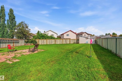 Expansive green lawn backyard featuring a patio area with pavers, perimeter wood fencing, and mature trees - 21207 90Ave, Edmonton, AB 