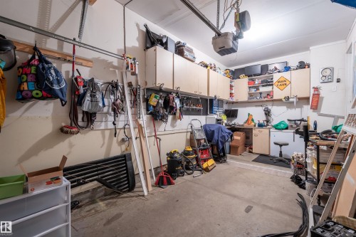 Spacious garage featuring concrete flooring, built-in cabinetry, overhead garage door system, and fluorescent lighting - 21207 90Ave, Edmonton, AB 