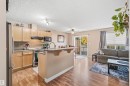 Open-concept living space featuring wood-finish flooring, a kitchen island with seating, stainless steel appliances, and wood cabinetry - 21207 90Ave, Edmonton, AB 