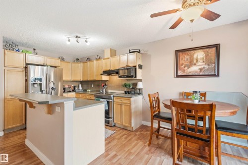 Kitchen featuring wood-finish flooring, light wood cabinetry, stainless steel appliances, a breakfast bar, and a dining area with a built-in bench - 21207 90Ave, Edmonton, AB 