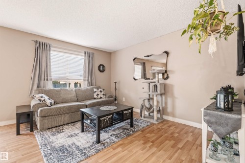 Living area featuring wood-finish flooring, neutral wall tones, and a large window with blinds and drapes - 21207 90Ave, Edmonton, AB 