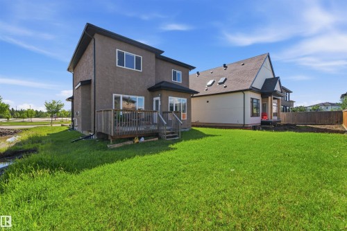 Expansive green lawn with a two-story stucco exterior and a raised wood-finish deck - 5110 Rue Eaglemont, Beaumont, AB 
