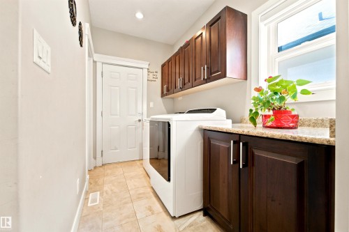 Laundry area featuring wood-finish cabinetry, a light-toned countertop, and tiled flooring - 5110 Rue Eaglemont, Beaumont, AB 