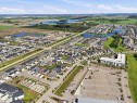 Aerial perspective showcasing a residential community with a mix of detached homes and multi-story buildings, featuring street parking, green spaces, and a large paved parking area - 5110 Rue Eaglemont, Beaumont, AB 