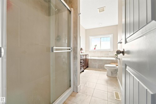 Bathroom featuring a glass-enclosed shower, a built-in soaking tub, a window above the tub, a vanity with a dark wood-finish cabinet, and light-toned tile flooring - 5110 Rue Eaglemont, Beaumont, AB 