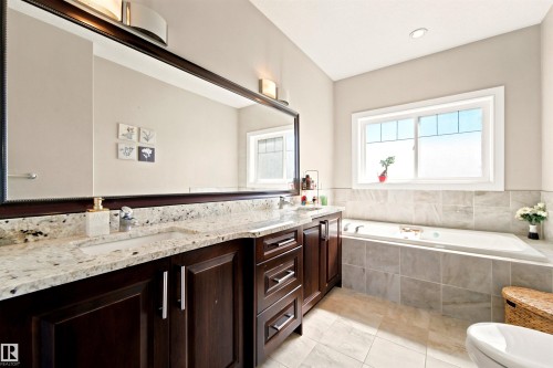 Dual vanity with stone countertop, large framed mirror, recessed lighting, and a built-in tub with tile surround - 5110 Rue Eaglemont, Beaumont, AB 
