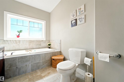 Spacious bathroom featuring a built-in soaking tub with tiled surround, a large window, light-toned wall paint, and coordinating floor tiles - 5110 Rue Eaglemont, Beaumont, AB 