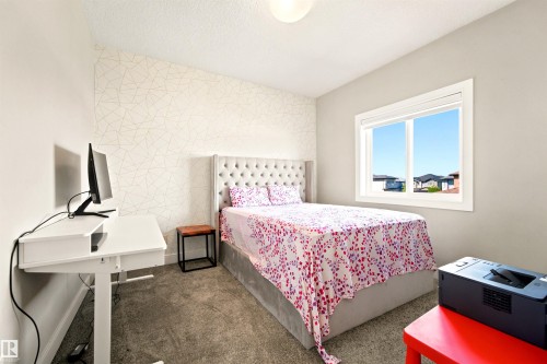 Bedroom featuring textured accent wall, plush carpeting, bright window, and a modern desk - 5110 Rue Eaglemont, Beaumont, AB 