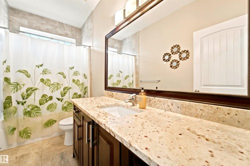 Spacious bathroom featuring a dark wood-finish vanity with a light-toned countertop, a large framed mirror, and a tiled shower surround with an integrated window - 5110 Rue Eaglemont, Beaumont, AB 