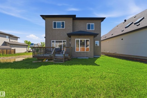 Back exterior featuring a large green lawn, multi-level wood deck, and a sunroom extension - 5110 Rue Eaglemont, Beaumont, AB 