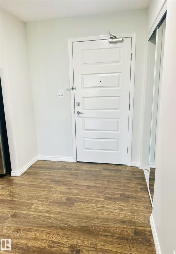 Entryway featuring wood-finish flooring, a paneled entry door, white baseboards, and a mirrored closet door - 318 646 Mcallister Loop, Edmonton, AB 