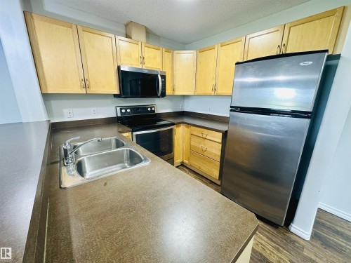 Kitchen featuring light wood-finish cabinetry, dark countertops, and stainless steel appliances - 318 646 Mcallister Loop, Edmonton, AB 