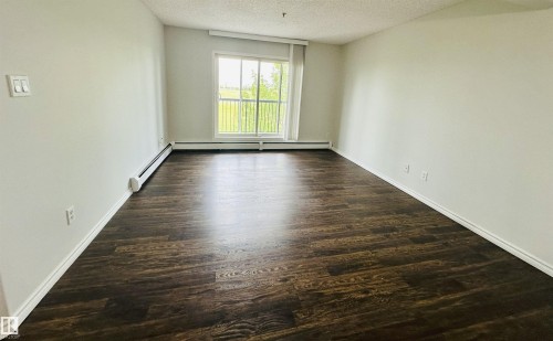 Expansive room featuring wood-finish flooring, white baseboards, and a large window - 318 646 Mcallister Loop, Edmonton, AB 