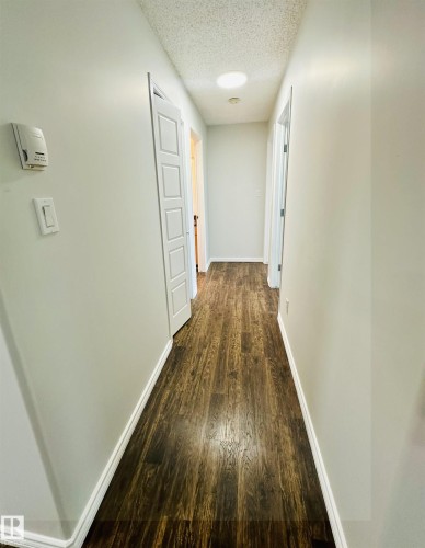 Hallway with wood-finish flooring, light grey walls, white trim, and white paneled doors - 318 646 Mcallister Loop, Edmonton, AB 
