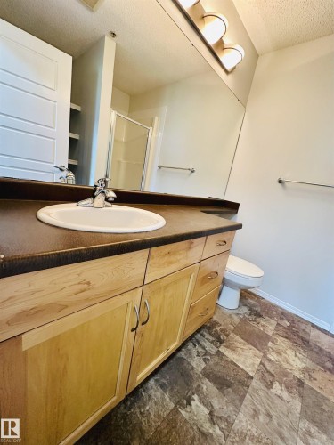 Wood-finish vanity with an integrated sink, dark countertop, and brushed nickel faucet - 318 646 Mcallister Loop, Edmonton, AB 