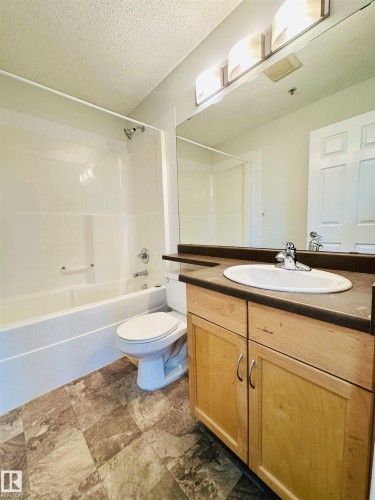 Bathroom featuring a vanity with a light wood-finish cabinet, dark countertop, and an undermount sink - 318 646 Mcallister Loop, Edmonton, AB 