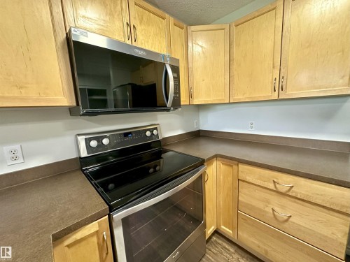 Kitchen featuring light wood cabinetry, dark countertops, and stainless steel appliances including a range and over-the-range microwave - 318 646 Mcallister Loop, Edmonton, AB 