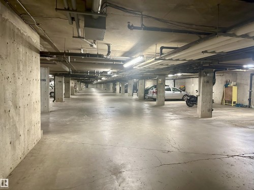 Underground parking garage featuring concrete pillars and ceiling, fluorescent lighting, and visible utility conduits - 318 646 Mcallister Loop, Edmonton, AB 
