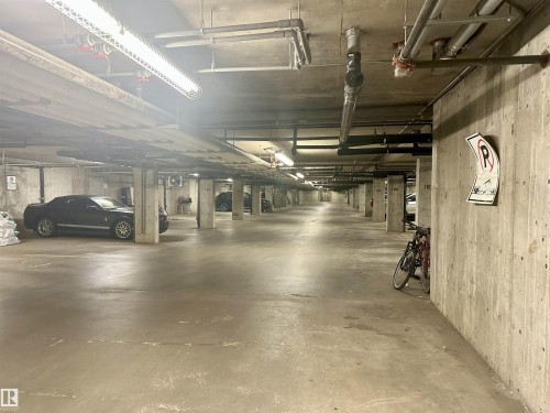 Underground parking facility featuring concrete walls and flooring, exposed ceiling utilities, and fluorescent strip lighting - 318 646 Mcallister Loop, Edmonton, AB 