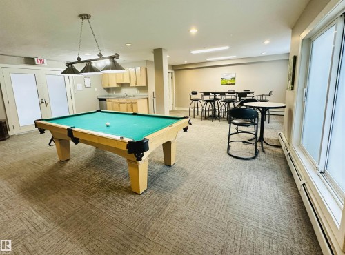 Recreation room featuring a pool table, patterned carpet flooring, and a compact kitchenette with light wood cabinetry - 318 646 Mcallister Loop, Edmonton, AB 