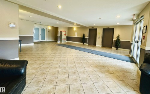 Spacious common area featuring large format tile flooring, recessed lighting, double elevators, and glass entry doors - 318 646 Mcallister Loop, Edmonton, AB 