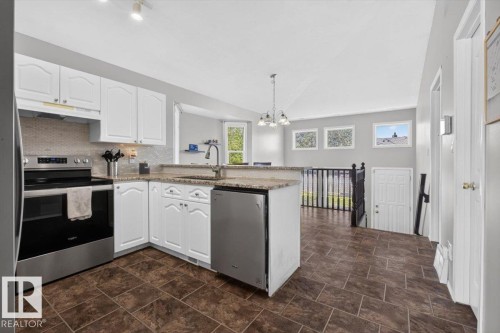 Kitchen featuring white cabinetry, stainless steel appliances, a stone-look countertop, and a tiled backsplash - 3907 33 Street, Edmonton, AB 