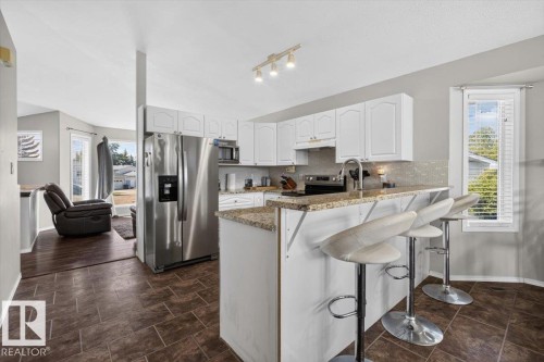 Kitchen featuring white cabinetry, stainless steel appliances, a bar-height counter with seating, and a tile-finish floor - 3907 33 Street, Edmonton, AB 