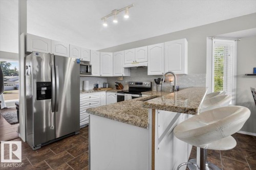 Kitchen featuring white cabinetry, light-toned granite countertops, a textured tile backsplash, stainless steel appliances, and track lighting - 3907 33 Street, Edmonton, AB 