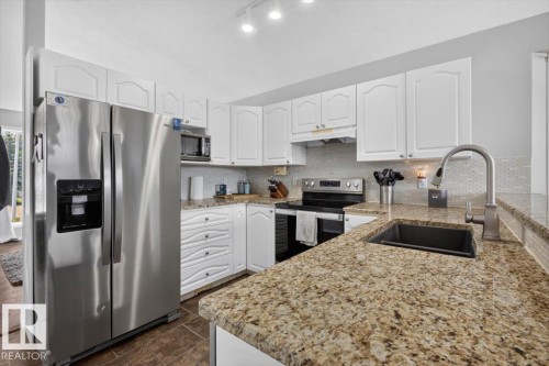 Kitchen featuring granite countertops, white cabinetry, stainless steel appliances, mosaic tile backsplash, and track lighting - 3907 33 Street, Edmonton, AB 