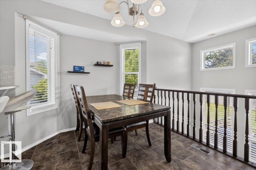 Dining area featuring tile flooring, multiple windows, a vaulted ceiling, and a dark wood-finish railing - 3907 33 Street, Edmonton, AB 