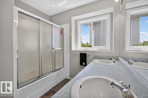 Bathroom featuring a dual vanity with integrated sinks, a patterned countertop, a window with exterior views, and a shower-over-tub with frosted sliding doors - 3907 33 Street, Edmonton, AB 