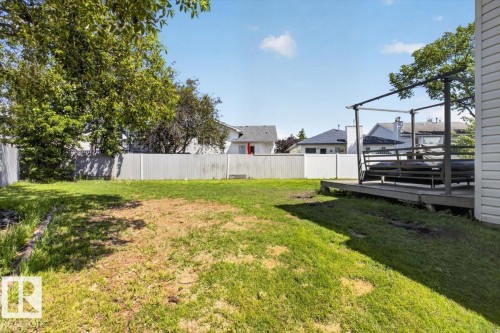 Expansive grassy backyard featuring a white privacy fence, mature trees, and a wooden deck with a built-in pergola frame - 3907 33 Street, Edmonton, AB 