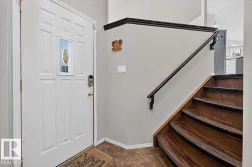 Entryway featuring a paneled door with decorative glass inlay, smart lock, tiled flooring, wood-finish staircase, and dark handrail - 3907 33 Street, Edmonton, AB 