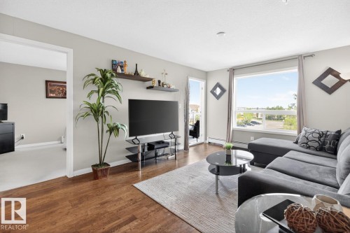 Spacious living area featuring wood-finish flooring, a large picture window, and a glass-paneled door opening to an outdoor space - 320 5005 165 Avenue, Edmonton, AB - Indoor Photo Showing Living Room