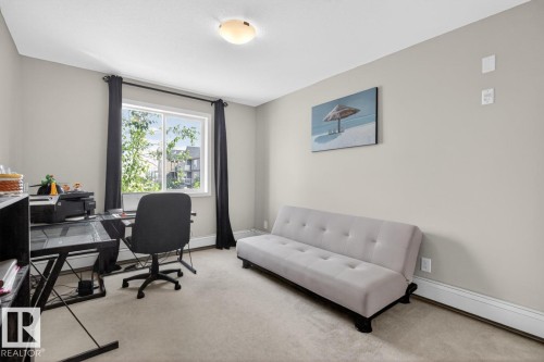 Carpeted interior room featuring a large window with dark drapes, light-toned walls, and a ceiling-mounted light fixture - 320 5005 165 Avenue, Edmonton, AB - Indoor Photo Showing Office