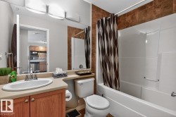 Bathroom featuring a built-in bathtub with shower, a vanity with a drop-in sink, wood-finish cabinetry, and a large mirror with integrated lighting - 