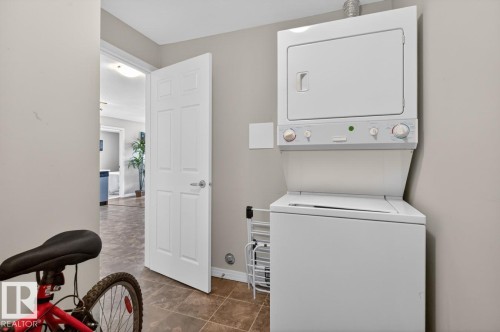 Integrated laundry area featuring a white stackable washer and dryer unit, tiled flooring, and neutral wall tones - 320 5005 165 Avenue, Edmonton, AB - Indoor Photo Showing Laundry Room