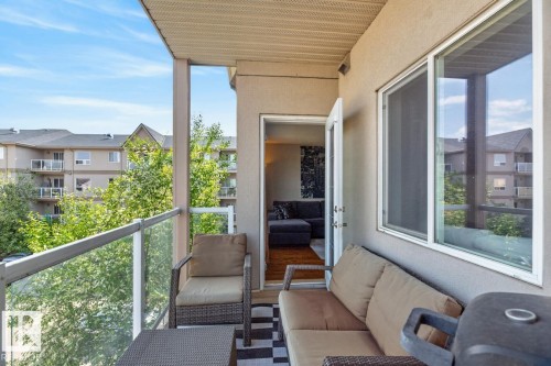 Private balcony featuring glass panel railings, textured exterior walls, and a white framed window - 320 5005 165 Avenue, Edmonton, AB - Outdoor With Balcony With Exterior