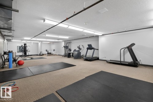 Fitness area featuring carpet flooring, overhead lighting, exposed ceiling pipes, and a selection of exercise equipment including treadmills and weight benches - 320 5005 165 Avenue, Edmonton, AB - Indoor Photo Showing Gym Room