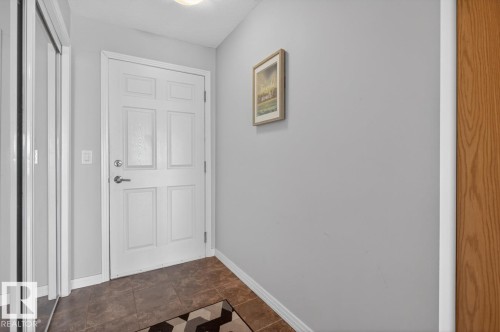 Entryway featuring a paneled door with brushed nickel hardware, slate-look tile flooring, and a sliding mirrored closet door - 320 5005 165 Avenue, Edmonton, AB - Indoor Photo Showing Other Room