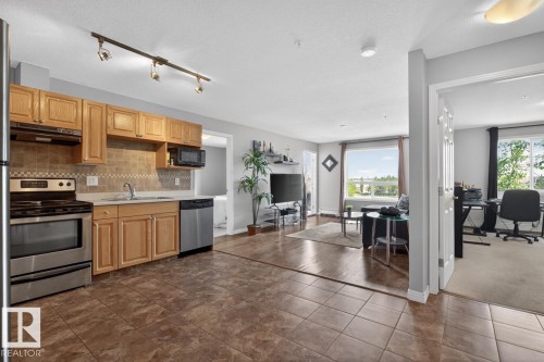Kitchen featuring wood cabinetry, stainless steel appliances, track lighting, and tiled flooring - 320 5005 165 Avenue, Edmonton, AB - Indoor Photo Showing Kitchen