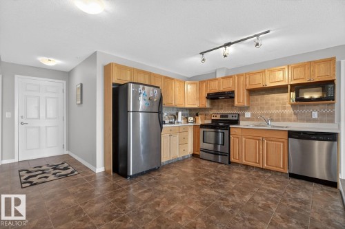Kitchen featuring wood cabinetry, stainless steel appliances, track lighting, and a tiled backsplash - 320 5005 165 Avenue, Edmonton, AB - Indoor Photo Showing Kitchen