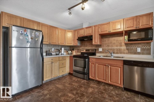 Kitchen featuring wood-finish cabinetry, stainless steel appliances, a tiled backsplash, and recessed lighting - 320 5005 165 Avenue, Edmonton, AB - Indoor Photo Showing Kitchen