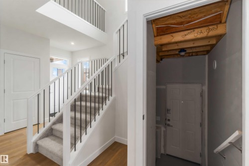 Grand entrance with a carpeted staircase featuring white risers and black iron balusters, wood-finish flooring, and a second-story landing with matching railing - 19360 29 Avenue, Edmonton, AB 