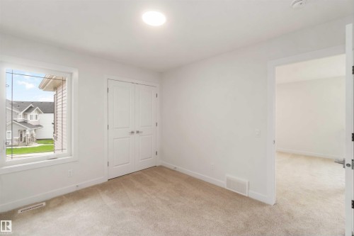 Carpeted interior space featuring a large window with white trim, a double-door closet, a flush-mounted ceiling light, and white walls - 19360 29 Avenue, Edmonton, AB 
